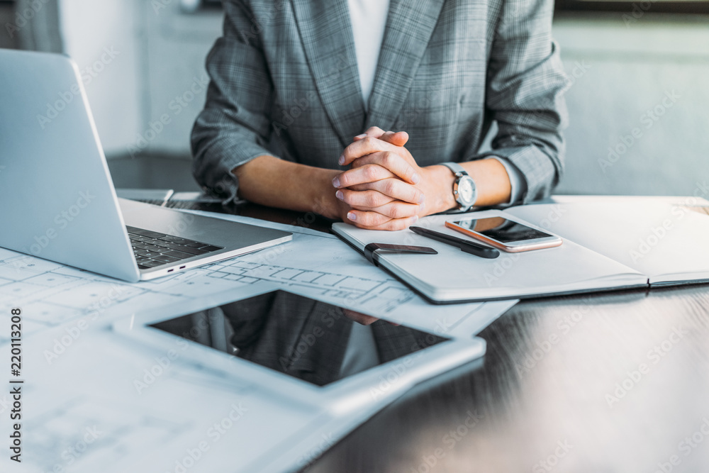 Fototapeta premium cropped image of businesswoman sitting at table in office with digital devices on tabletop