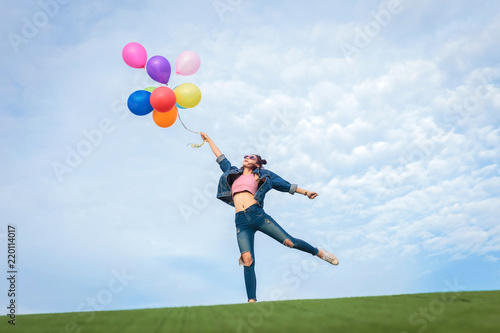 Asain woman holding colorful balloons and jumping in to blue sky and white clouds background.