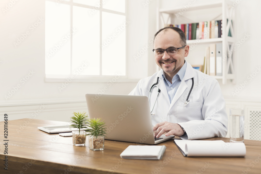 Portrait of doctor in glasses sitting at desktop