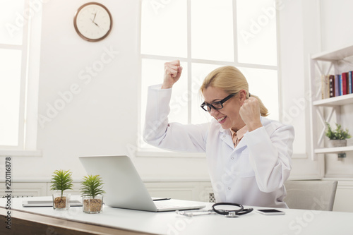 Excited doctor in glasses sitting at desktop