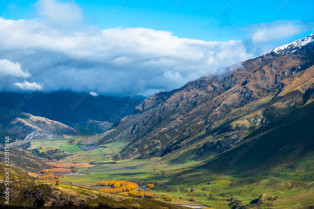 Stunning landscape view of green grass field and snow mountain in autumn on a cloudy day. Diamond lake track, Wanaka, New Zealand.