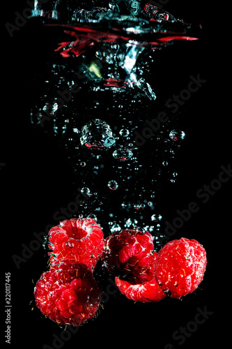 Closeup shot of ripe raspberry covered with air bubbles and falling down in water on black background