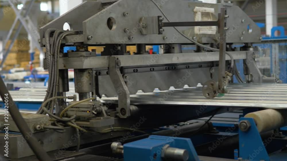 The machine cuts a sheet of metal. Factory for the creation of metal roofing. Rolling metal in the machine to create a metal roof. The machine cuts a sheet of metal. Factory for the creation of metal roofing. Rolling metal in the machine to create a metal roof.