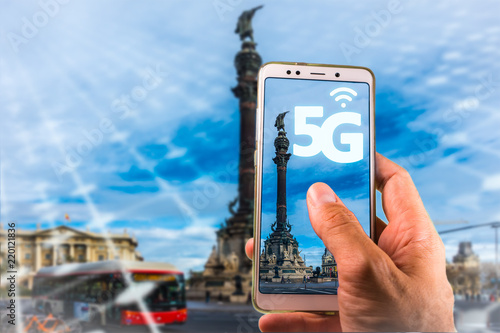 Smartphone with 5G on screen and Famous Columbus Monument, Colon, in Barcelona on the background