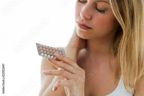 Beautiful young woman holding contraceptive pills over white background.
