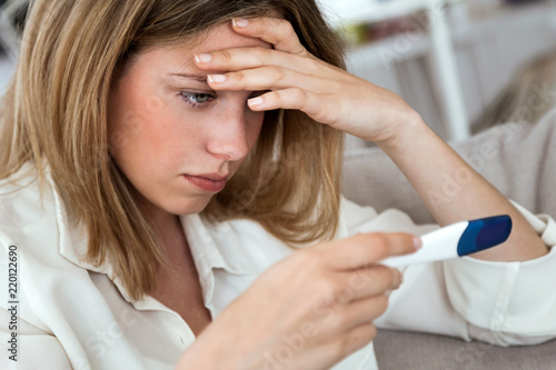 Young woman feeling depressed and sad after looking at pregnancy test result at home.