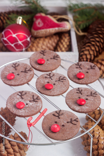 Chocolate festive cookies in the form of a deer Rudolph with a red nose surrounded by festive decor.