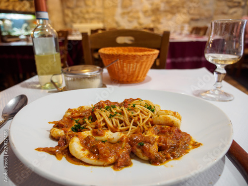Wide closeup of a plate of squid seafood bolognese spaghetti with a glass of white wine at a table at an Italian restaurant, Paris, France. Travel and cuisine.