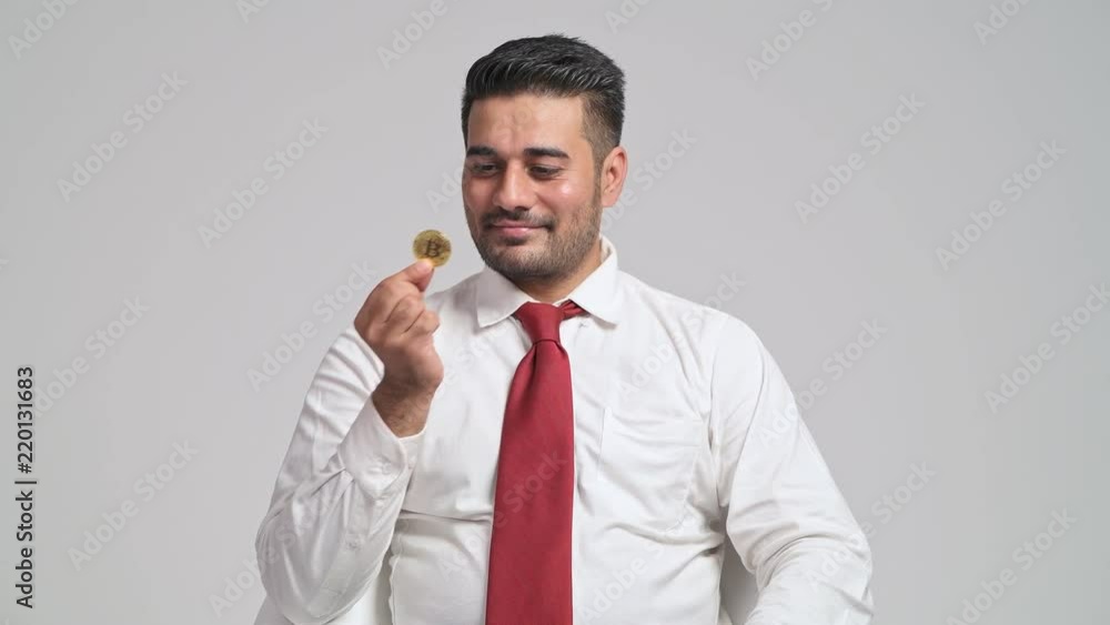 Bitcoin trading concept. Young indian business man holding a golden bitcoin, kissing it and smile. Cryto currency, bitcoin online trading and transaction finance concept. Bitcoin trading concept. Young indian business man holding a golden bitcoin, kissing it and smile. Cryto currency, bitcoin online trading and transaction finance concept.