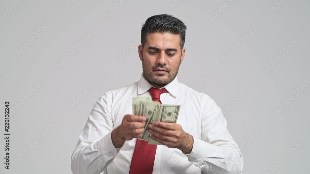 Businessman counting cash in white background. Young indian man in white shirt and red tie happy counting dollar in front to camera. Bribery concept. Businessman counting cash in white background. Young indian man in white shirt and red tie happy counting dollar in front to camera. Bribery concept.