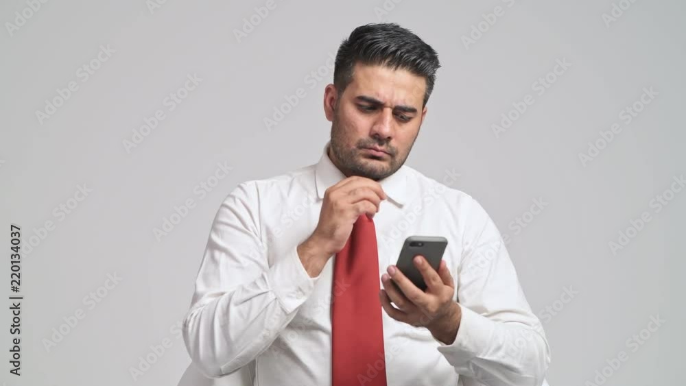 Businessman using mobile phone portrait. Young indian man with red tie using mobile device, browsing for messages, very upset. Mobile office concept. Businessman using mobile phone portrait. Young indian man with red tie using mobile device, browsing for messages, very upset. Mobile office concept.