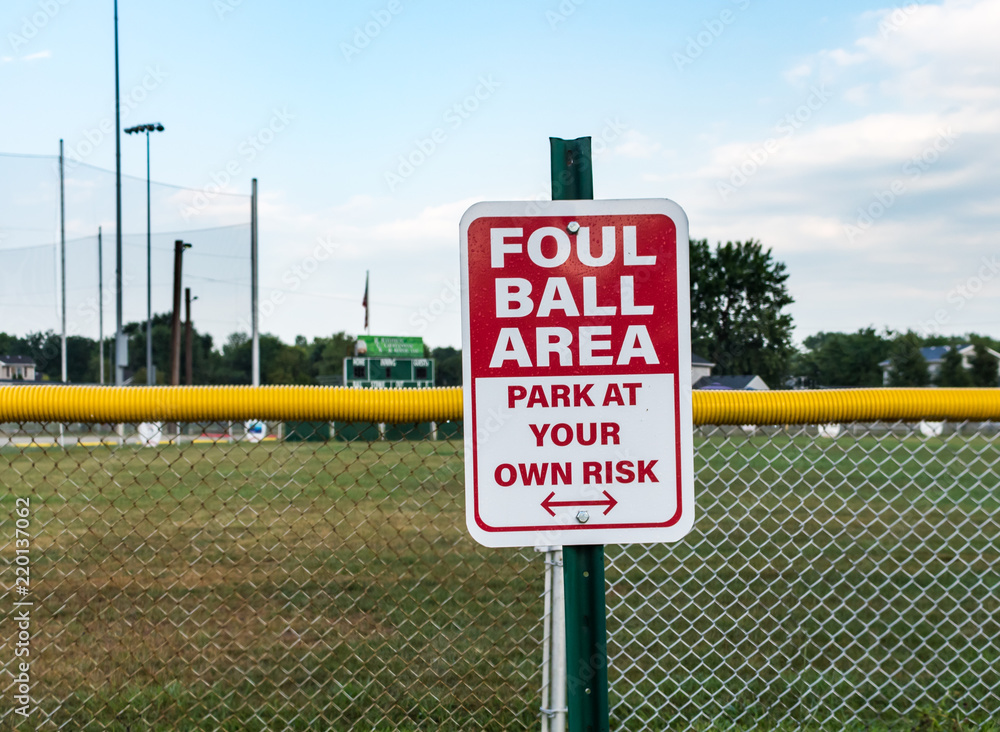 Sign at children's baseball field, warning Foul Ball Area. Red and