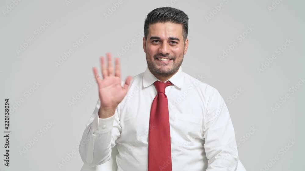 Confident businessman portrait in white background. Young indian man in white shirt and red tie pose waving hand to camera. Young businessman concept. Confident businessman portrait in white background. Young indian man in white shirt and red tie pose waving hand to camera. Young businessman concept.