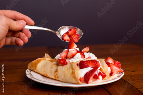 Golden crepes with strawberries and whipped cream with strawberries being spooned on-top. photo