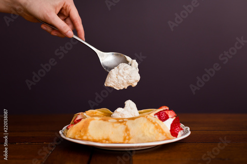 Golden crepes with strawberries and whipped cream with whipped cream being spooned on-top. photo