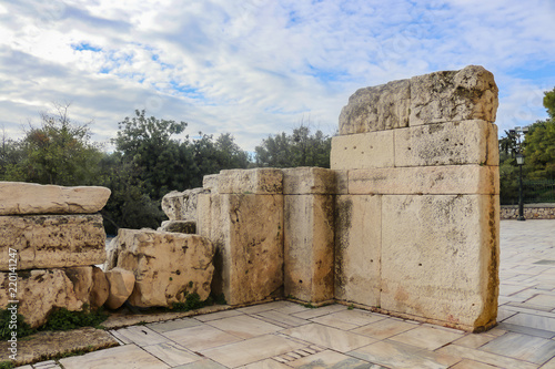 Fototapeta Naklejka Na Ścianę i Meble -  Chunks of marble forming a wall near the Athens Parthenon with trees and a blue cloudy sky behind