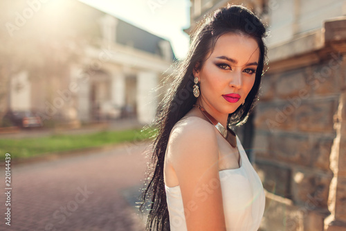 Beautiful woman with long hair wearing white wedding dress outdoors. Beauty fashion model with jewelry and makeup