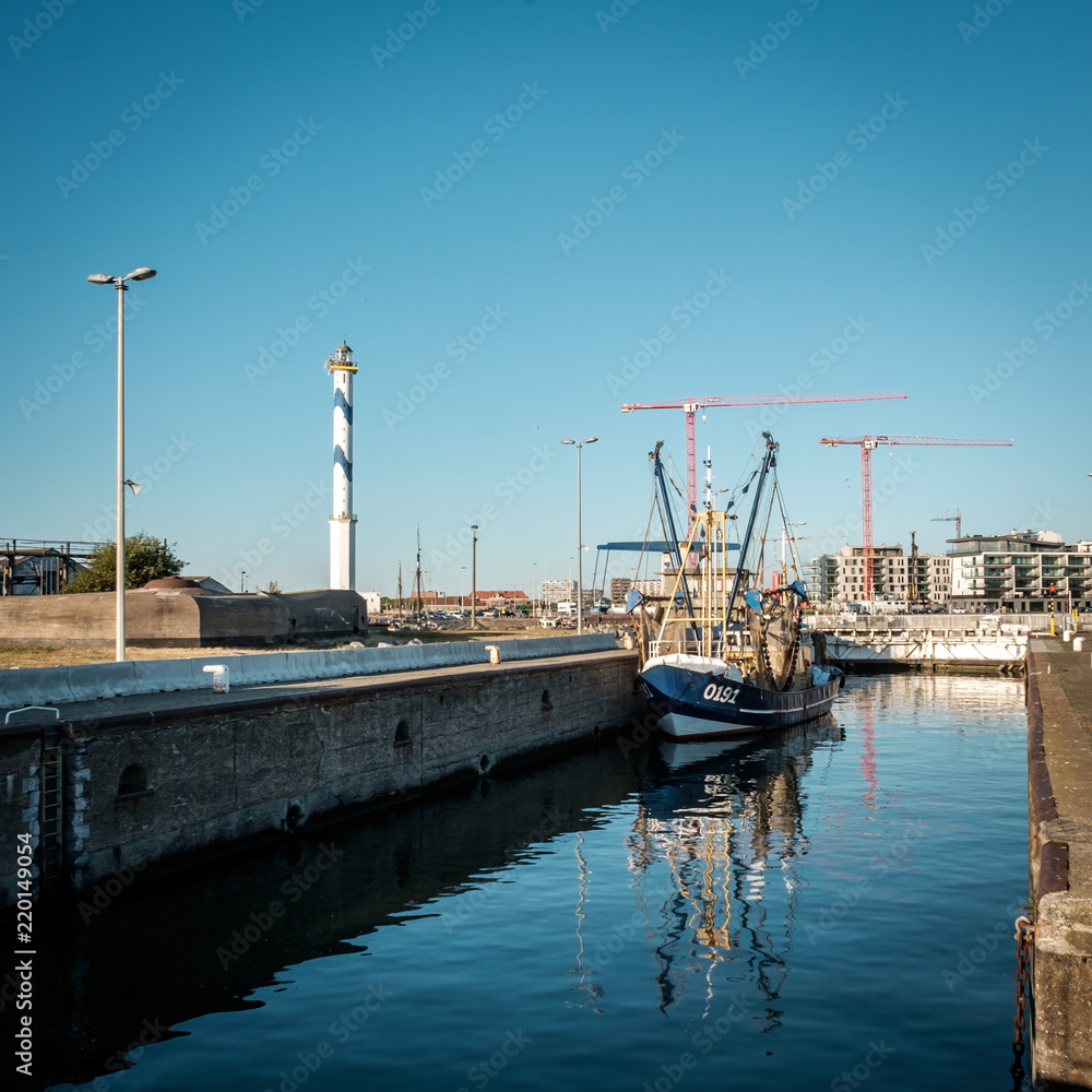 Fishing boat and old lighthouse of Ostend reflected in the water of a lock Fishing boat and old lighthouse of Ostend reflected in the water of a lock