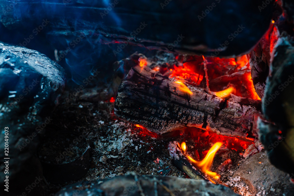 Smoldered logs burned in vivid fire. Atmospheric background with orange flame of campfire. Unimaginable detailed image of bonfire from inside with copy space. Smoke and ashes close up. Smoldered logs burned in vivid fire. Atmospheric background with orange flame of campfire. Unimaginable detailed image of bonfire from inside with copy space. Smoke and ashes close up.