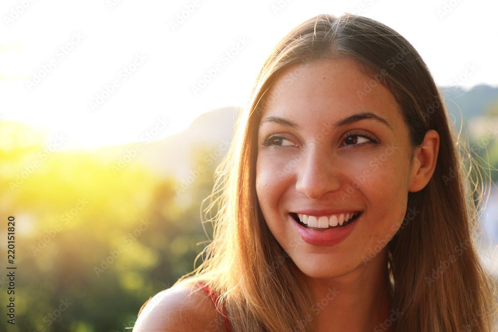 Woman smiling with perfect smile and white teeth thinking and looking sideways in park in summer. Sunlight flare. Copy space. Woman smiling with perfect smile and white teeth thinking and looking sideways in park in summer. Sunlight flare. Copy space.