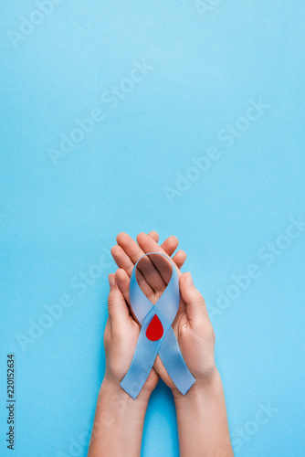 the blue ribbon awareness with red blood drop in woman hands isolated on a blue background. World diabetes day,14 november. Copy space. Top view