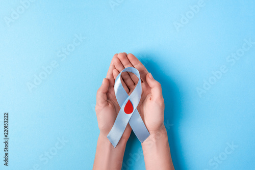 the blue ribbon awareness with red blood drop in woman hands isolated on a blue background. World diabetes day,14 november. Copy space. Top view