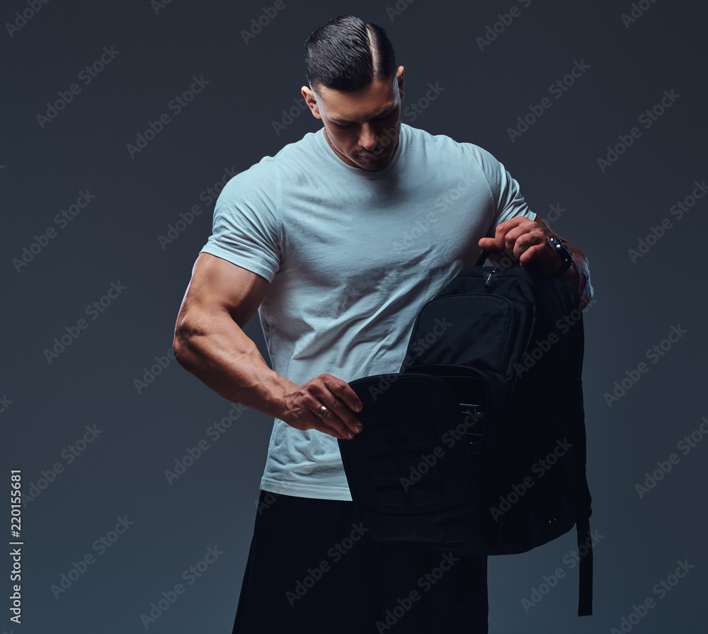 Muscular handsome bodybuilder in sportswear with rucksack looks into an  open backpack in a studio against a gray background. Stock-Foto | Adobe  Stock