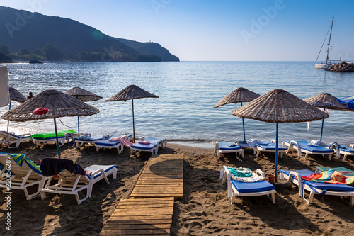 An empty beach in a heavenly bay. Beach umbrellas with sunbeds and towels on towels. Sea and sky background. photo