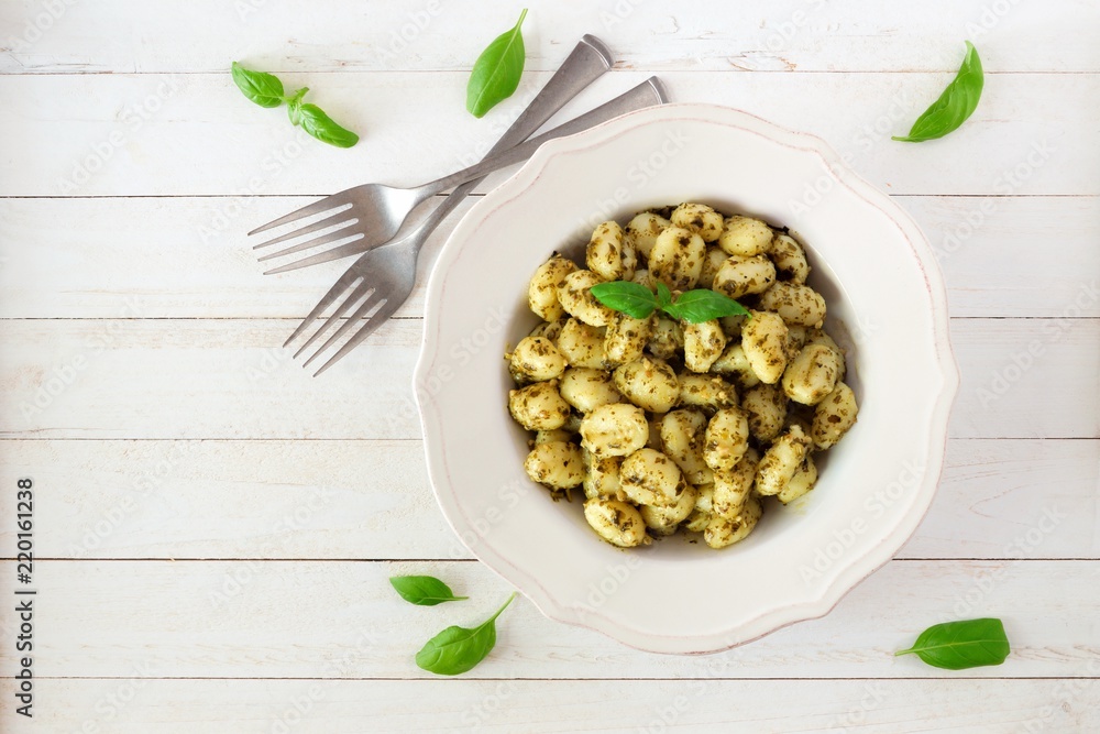 Plate of gnocchi with pesto sauce. Top view over a white wood background.