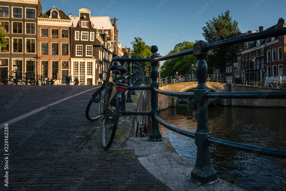 A lonely bicycle tied to a canal fence in the city of Amsterdam at sunset, the Netherlands
