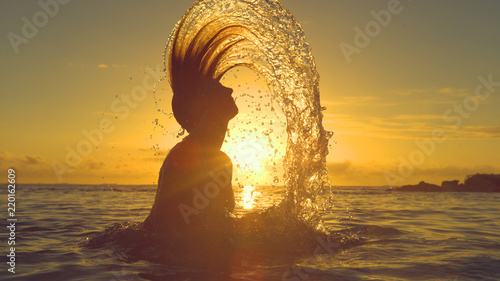 SILHOUETTE Young woman sprays refreshing water by whipping her head out of ocean photo