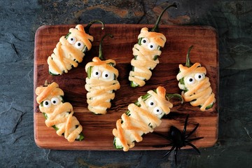 Homemade Halloween mummy jalapeno poppers, top view on wooden server with spiders
