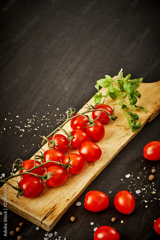 delicious and juicy cherry tomatoes and basil on a wooden board on a black table delicious and juicy cherry tomatoes and basil on a wooden board on a black table
