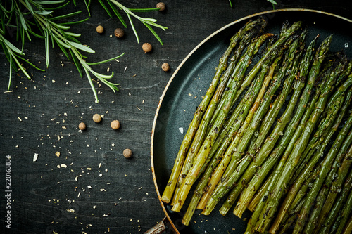 delicious green asparagus in a pan on a wooden black table with rosemary and salt