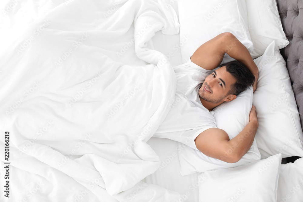 Young man lying in bed with soft pillows at home, top view Young man lying in bed with soft pillows at home, top view