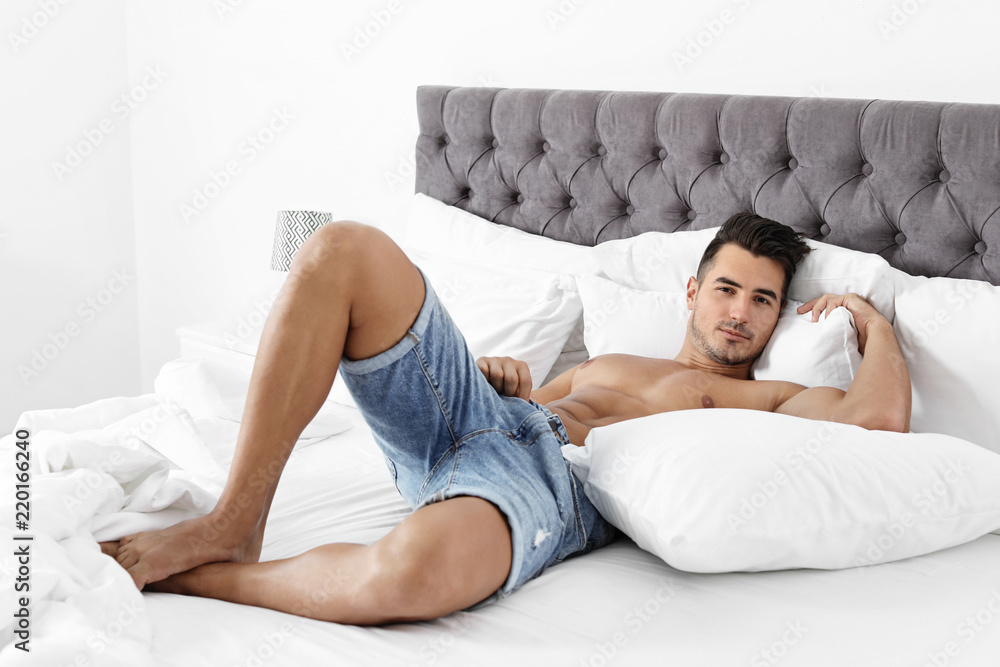 Sexy young man lying on bed with soft pillows at home Sexy young man lying on bed with soft pillows at home