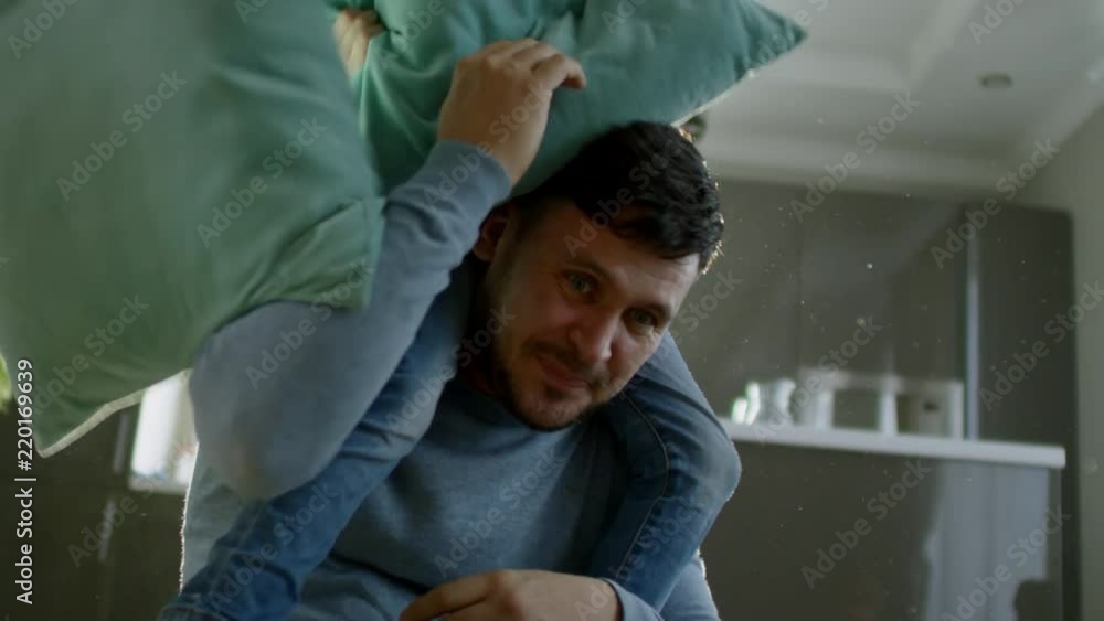 Medium shot of playful little girl of primary school age riding on father’s shoulders during pillow fight with family at home Medium shot of playful little girl of primary school age riding on father’s shoulders during pillow fight with family at home
