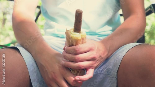 a young lonely guy holding a hotdog, in the lower abdomen, sitting on a bench in the park, and open the hotdog packaging, imitating an erection . 4k, slow-motion