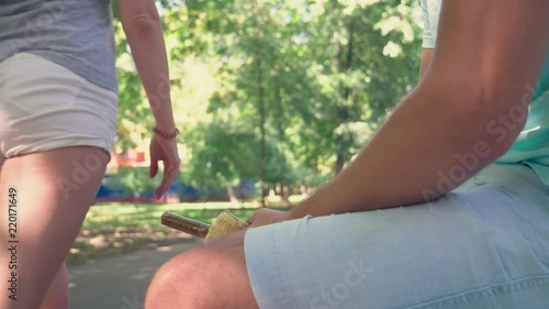 a young lonely guy holding a hotdog, in the lower abdomen, sitting on a bench in the park, and open the hotdog packaging, imitating an erection . 4k, slow-motion