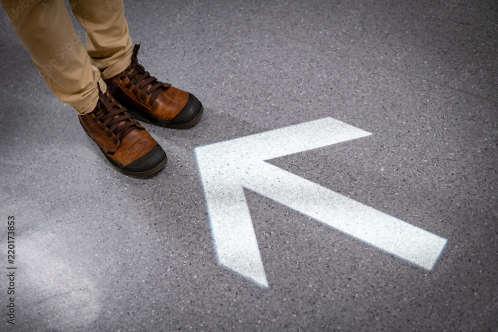 Male feet with casual shoes standing at the end of light arrowhead sign on the floor. Keep moving forward concept. Urban lifestyle fashion. Male feet with casual shoes standing at the end of light arrowhead sign on the floor. Keep moving forward concept. Urban lifestyle fashion.