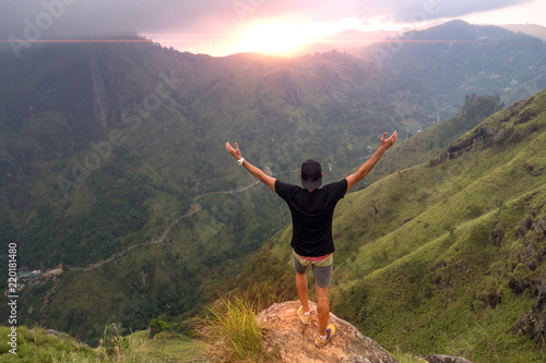 Hiker standing on top of a mountain with raised hands and enjoying sunrise