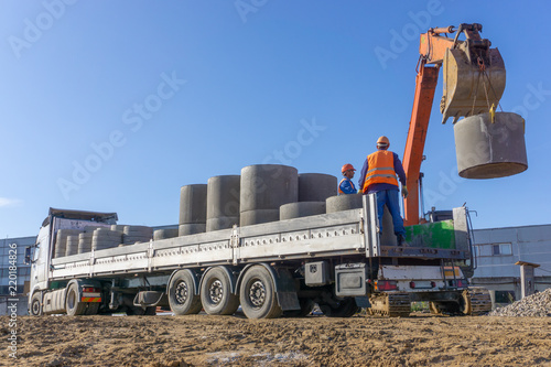 Delivery and unloading of construction materials by the excavator to the construction site. Concrete rings and elements for a well.