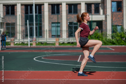 Red-haired young girl runs in the stadium. Student delivers standards for running outdoors. Young woman running on the football field