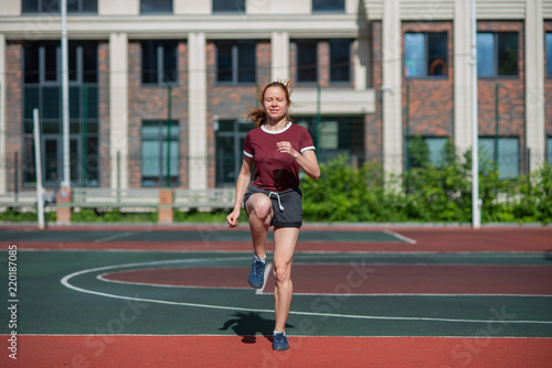 Red-haired young girl runs in the stadium. Student delivers standards for running outdoors. Young woman running on the football field