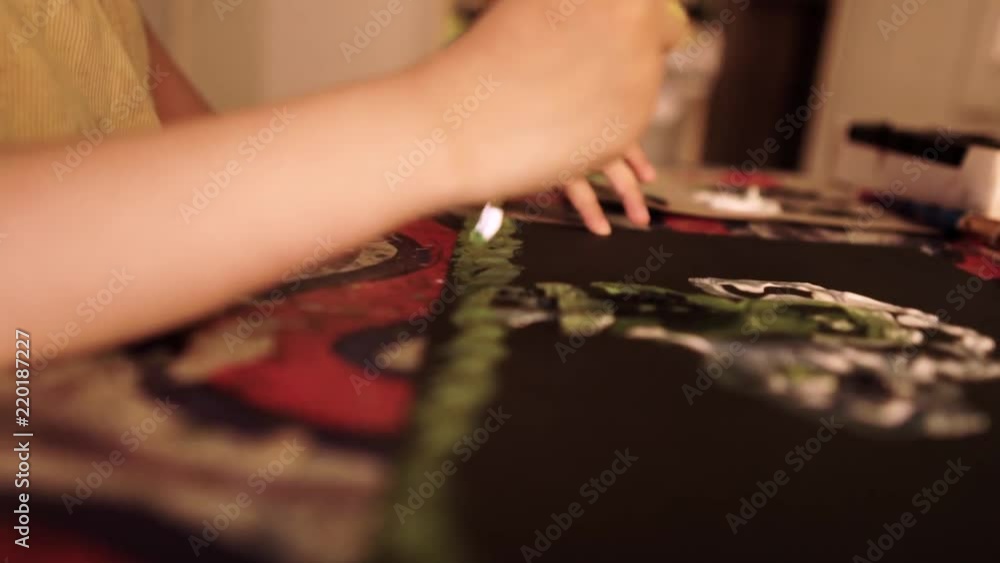 Young girl painting alone in dimly lit room on colorful table shot in close up and and artistic way using slow motion Young girl painting alone in dimly lit room on colorful table shot in close up and and artistic way using slow motion