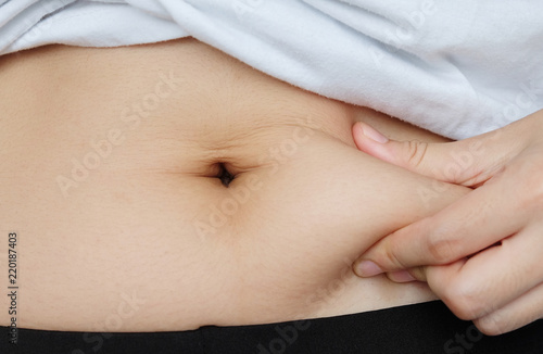 Side of woman hand catching fat body belly paunch , diabetic risk factor . © Konkapp