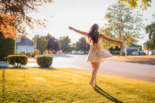 a woman in a dress twirling on a suburban front lawn in the summer at golden hour