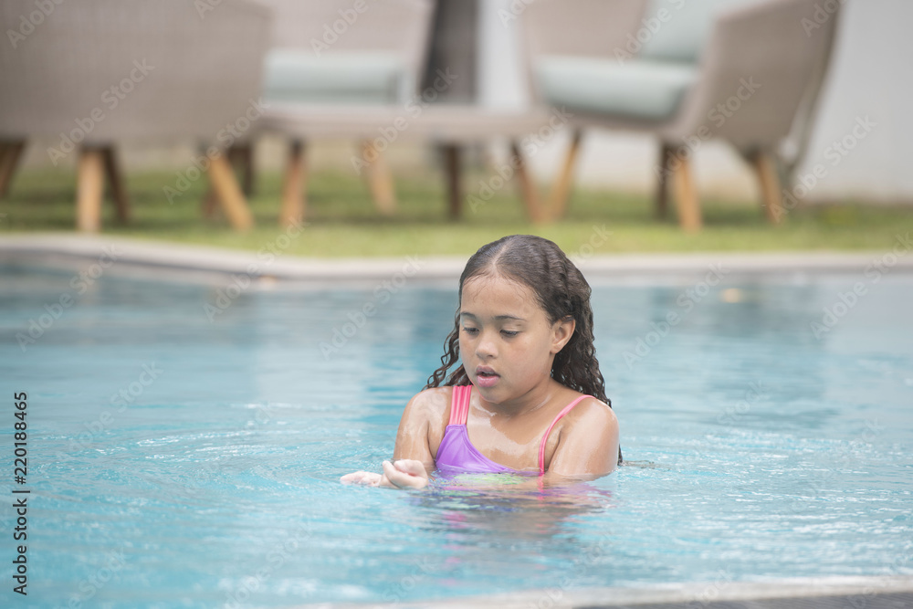 Young child relaxing, swimming and playing calmly in a pool showing her wet curly hair