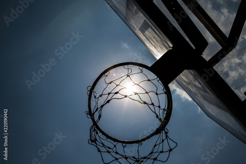Siluate basketball hoop under the sun and blue sky