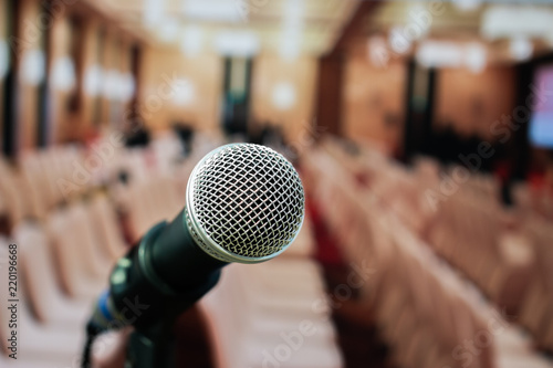 Microphones on abstract blurred of speech in seminar room or front speaking conference hall light, white chairs for people in event meeting convention hall in hotel.